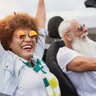Trendy senior couple having fun inside convertible car - Multiracial mature people on a road trip with cabriolet car stock photo