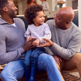 Grandfather With Father And Son Sit On Step At Home Putting On Boots Before Going On Family Walk
